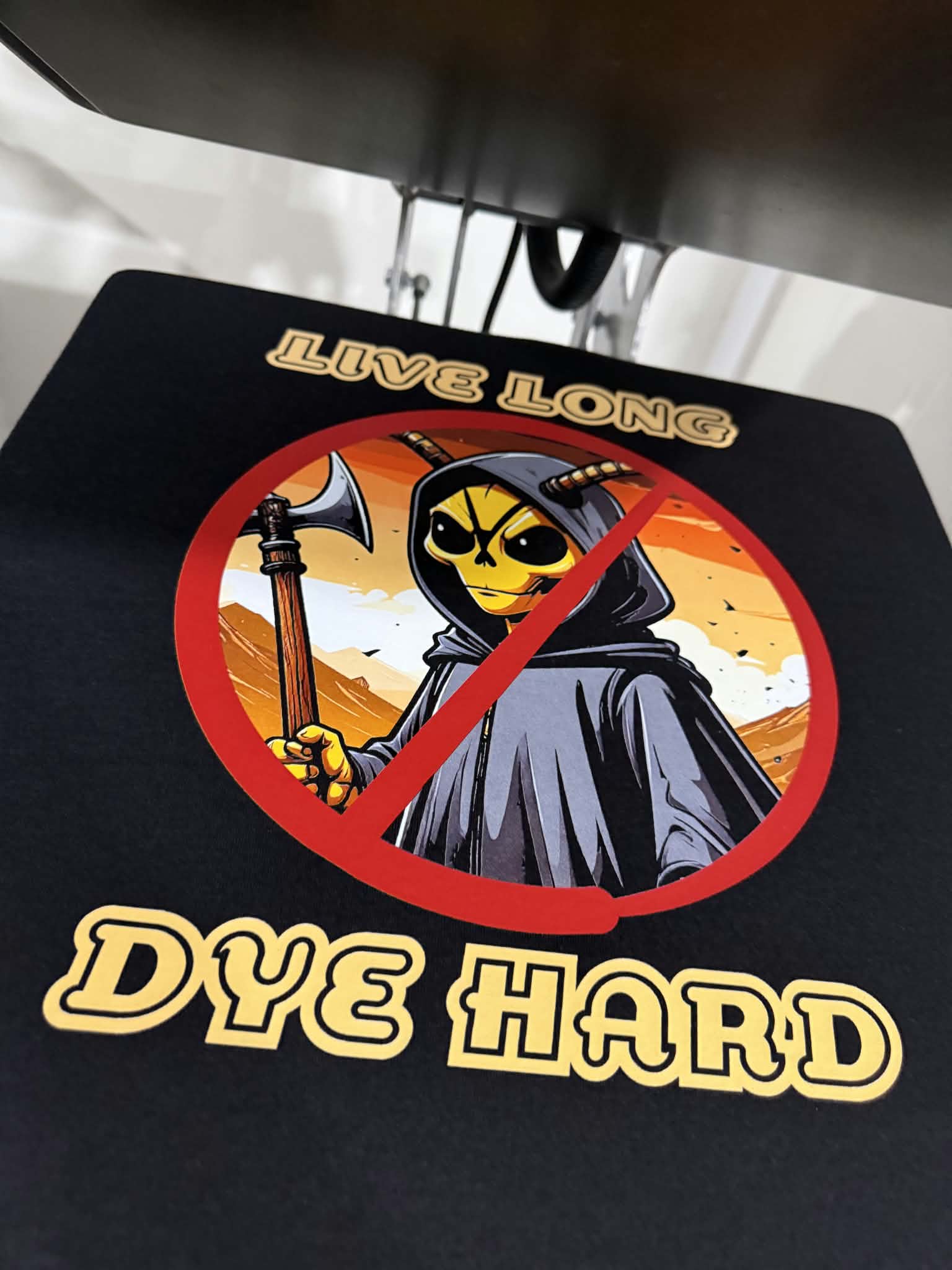 Un transfert &laquo;&nbsp;Live Long Dye Hard&nbsp;&raquo; press&eacute; &agrave; chaud sur un chandail noir, la presse encore ouverte au-dessus.