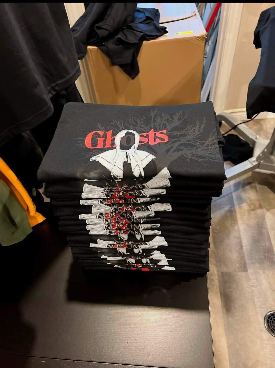 Une commande prête à livrer dans l'atelier : une pile de t-shirts noirs fraîchement imprimés du visuel « Ghosts », pliés sur la table de travail.